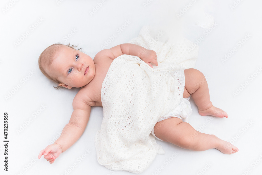 Happy baby girl lies on a white sheet in her room Happy baby girl lies on a white sheet in her room