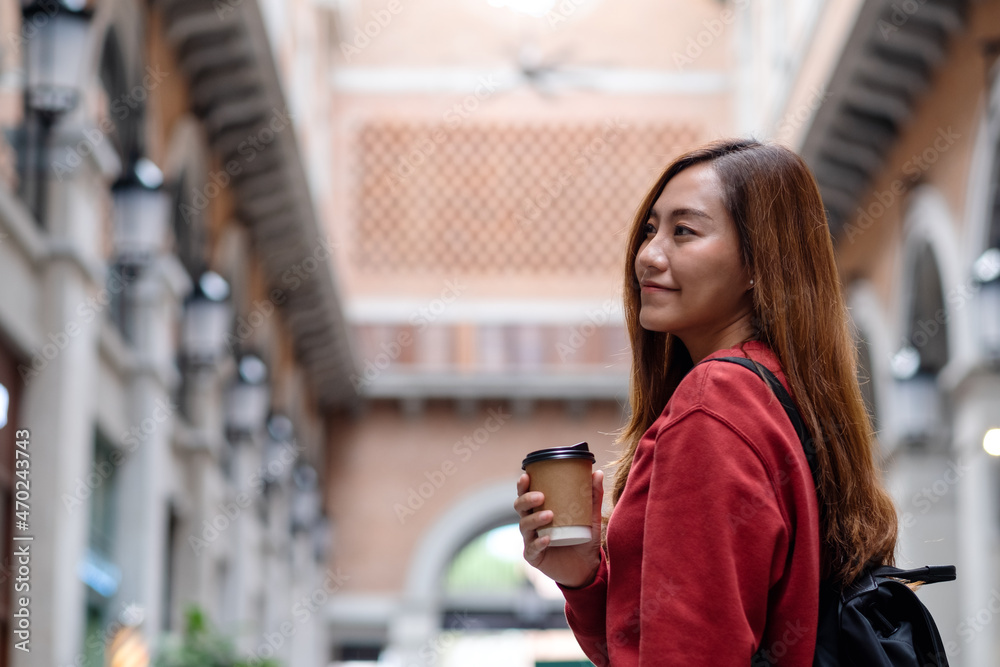 A young asian woman holding coffee cup and walking on the street while traveling and sightseeing around the city