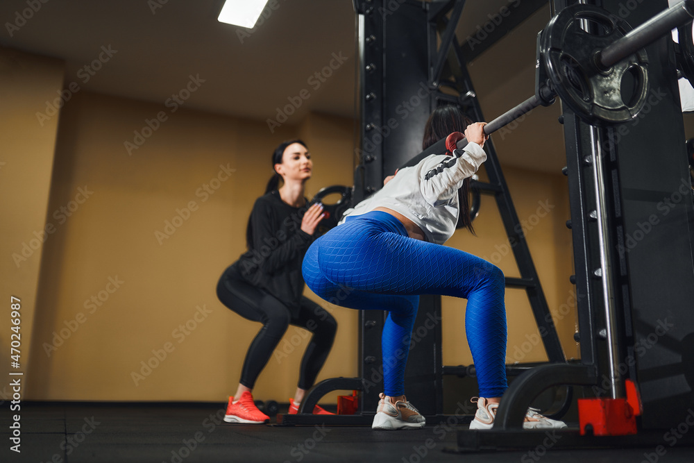 Young caucasian woman working out legs with barbell In gym with instructor. Personal female trainer