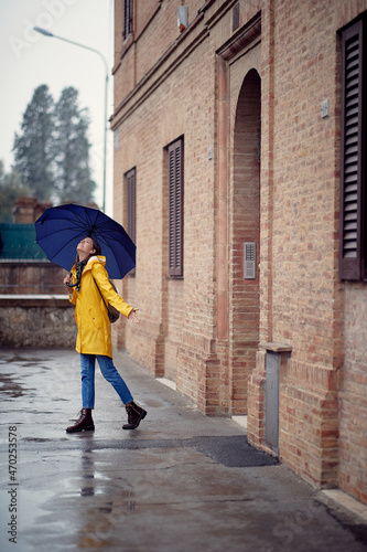 A young handsome woman in a yellow raincoat and with umbrella is happy about rain while walking the city. Walk, rain, city