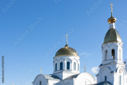 The Christian church is white with golden domes and crosses on a blue sky background. Orthodox architecture with elements of golden color.