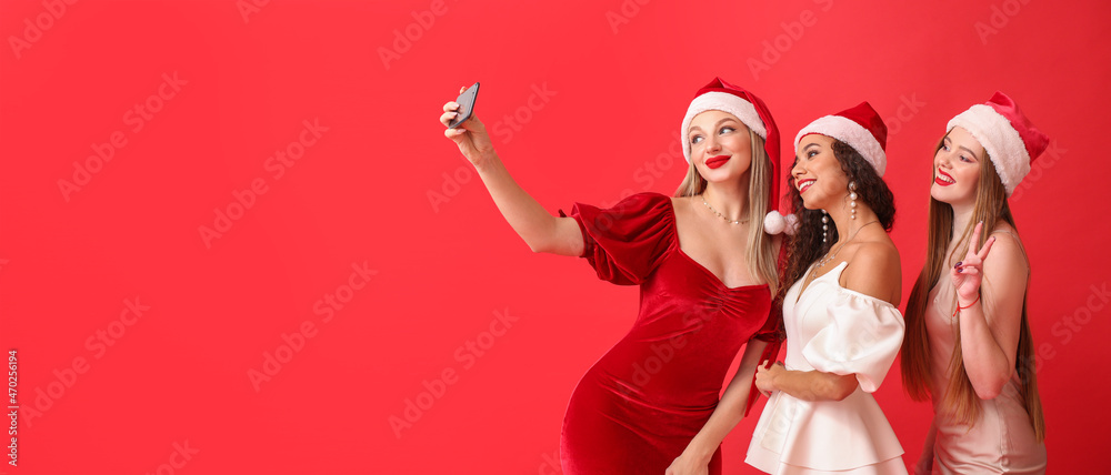 Beautiful young women in Santa hats taking selfie on color background with space for text