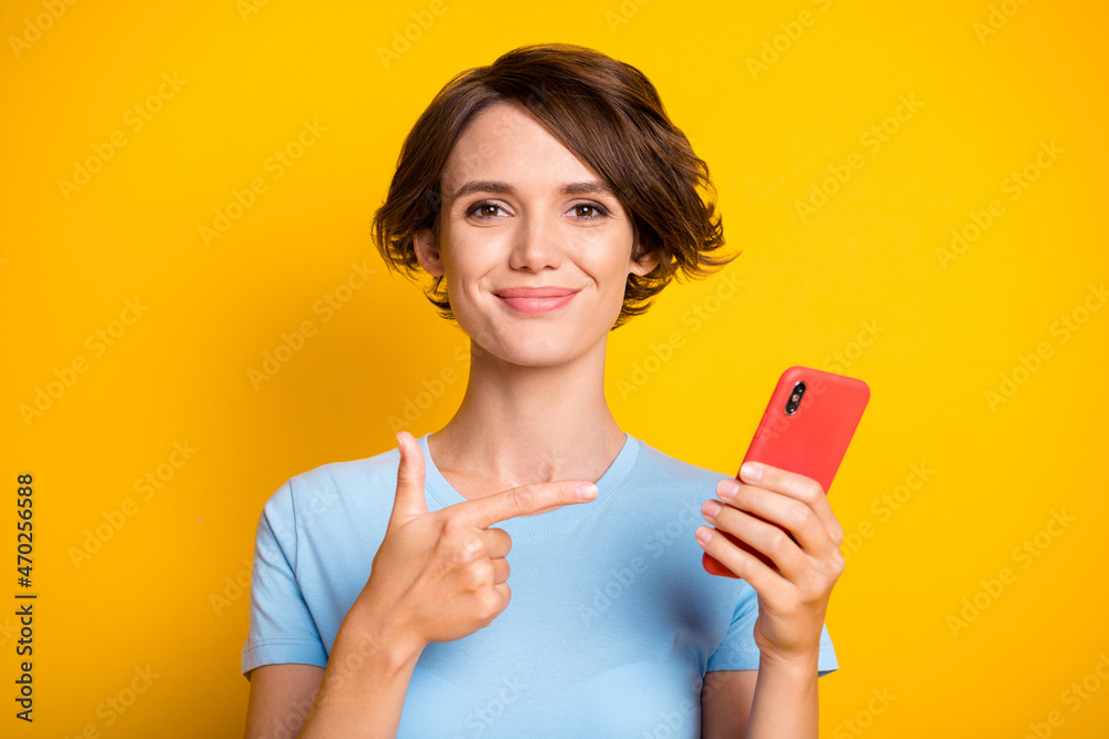 Photo of young girl happy positive indicate finger cellphone ad promo recommend isolated over yellow color background Photo of young girl happy positive indicate finger cellphone ad promo recommend isolated over yellow color background
