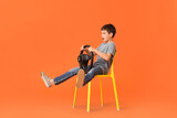 Surprised little boy with steering wheel sitting in chair on color background