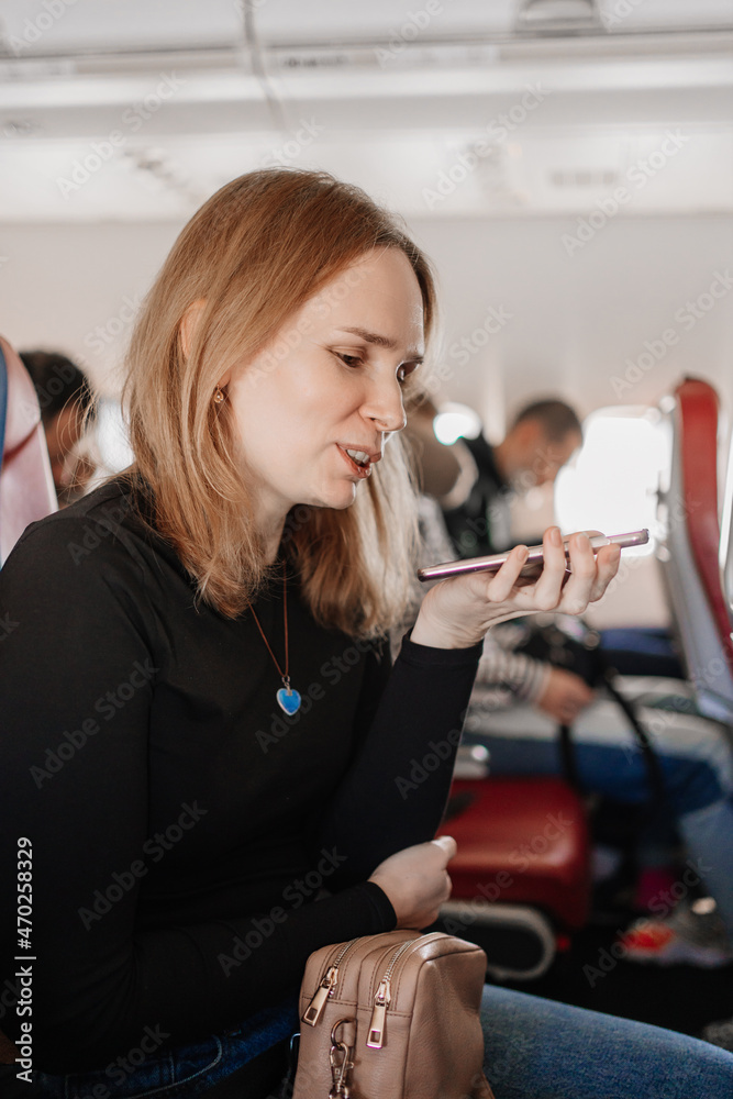 woman is records a voice message on the phone in a seat on board the plane. 