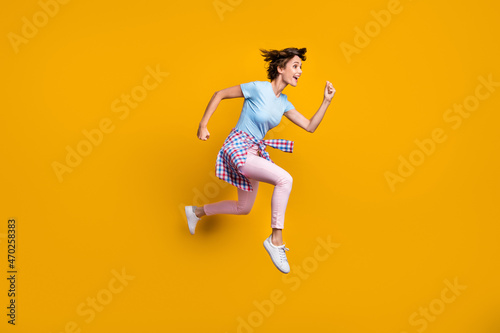 Fototapeta Naklejka Na Ścianę i Meble -  Photo portrait full side body view of running girl with tight waist shirt jumping up isolated on vivid yellow colored background