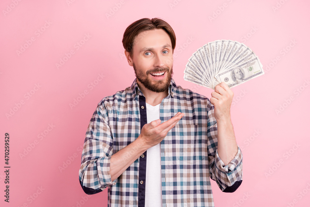 Photo of young man happy positive smile show hand money cash dollars rich isolated over pink color background Photo of young man happy positive smile show hand money cash dollars rich isolated over pink color background