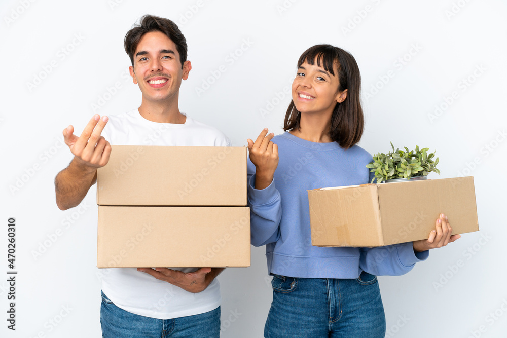 Young couple making a move while picking up a box full of things isolated on white background inviting to come with hand. Happy that you came Young couple making a move while picking up a box full of things isolated on white background inviting to come with hand. Happy that you came
