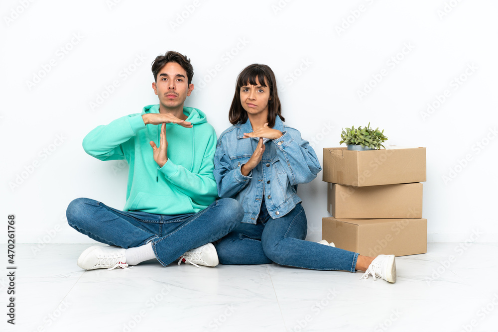 Young couple making a move while picking up a box full of things sitting on the floor isolated on white background making stop gesture with her hand to stop an act Young couple making a move while picking up a box full of things sitting on the floor isolated on white background making stop gesture with her hand to stop an act