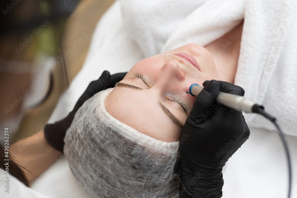 Fototapeta premium Therapist beautician makes a laser treatment to young woman's face at beauty SPA clinic. Close-up process of laser removal of blood vessels from the skin