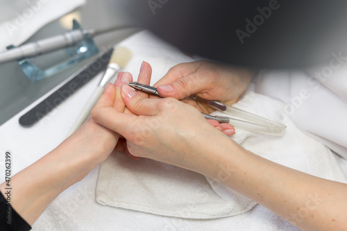 Close-up finger nail care by manicure specialist in beauty salon. Manicurist clear cuticle with professional scissors for manicure
