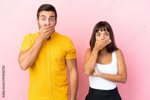 Young couple isolated on pink background covering mouth with hands for saying something inappropriate
