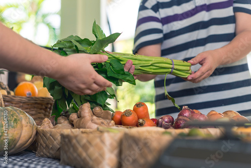 A man hands over a bundle of Water Spinach or Kangkong to a vendor. Buying fresh vegetables at a small market stall. photo