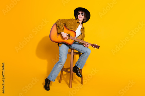 Photo of funky charming woman dressed cowboy clothes spectacles sitting bar singing playing guitar isolated yellow color background © deagreez