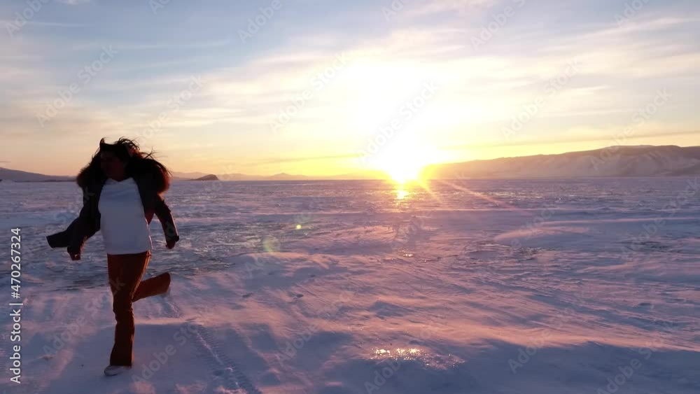 Lake Baikal. The girl runs along the frozen lake towards the sunset. Evening shooting on Ogoy Island. Lake Baikal. The girl runs along the frozen lake towards the sunset. Evening shooting on Ogoy Island.