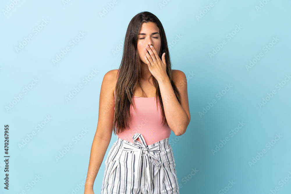 Young brazilian woman isolated on blue background yawning and covering wide open mouth with hand Young brazilian woman isolated on blue background yawning and covering wide open mouth with hand
