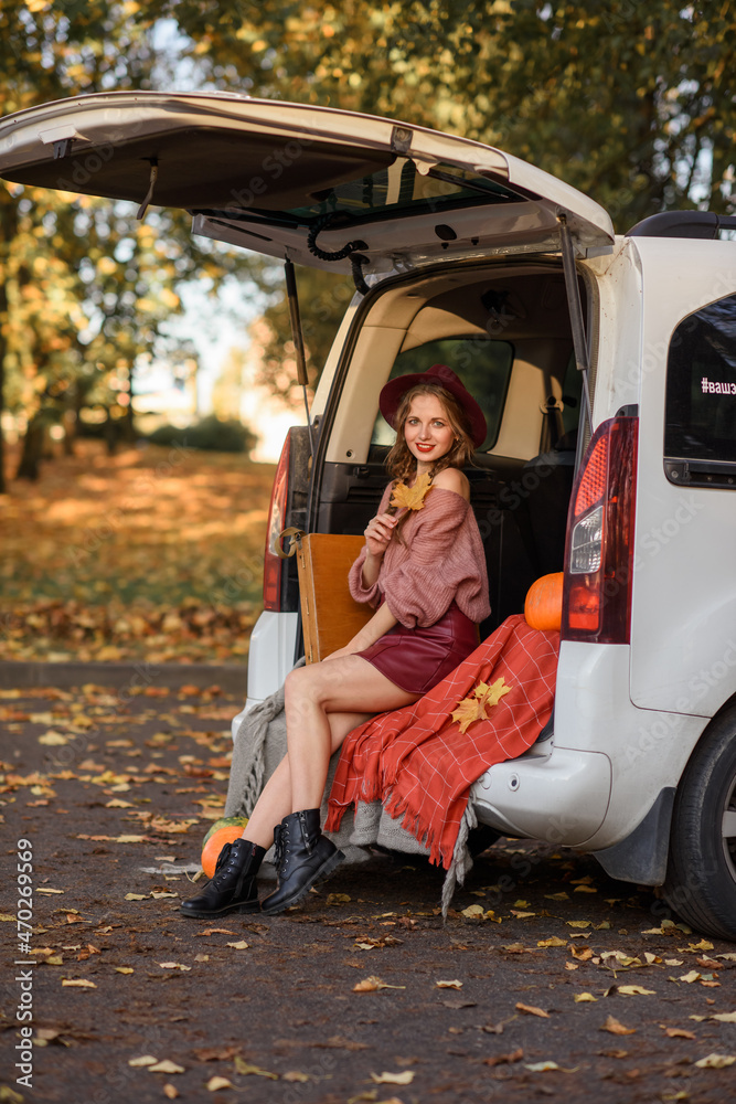 beautiful caucasian girl sitting in a car in the fall in a sweater hat and short skirt. Near easel