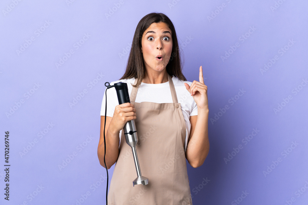 Brazilian woman using hand blender isolated on purple background intending to realizes the solution while lifting a finger up Brazilian woman using hand blender isolated on purple background intending to realizes the solution while lifting a finger up