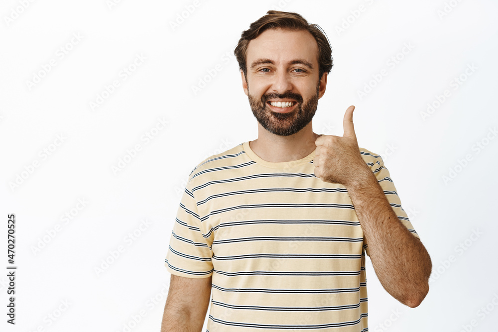 Fototapeta premium Smiling bearded man showing thumbs up in approval, like and agree, standing in t-shirt over white background