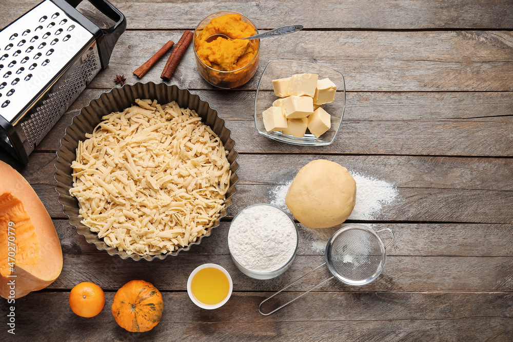 Baking dish with uncooked pumpkin pie and ingredients on wooden background Baking dish with uncooked pumpkin pie and ingredients on wooden background