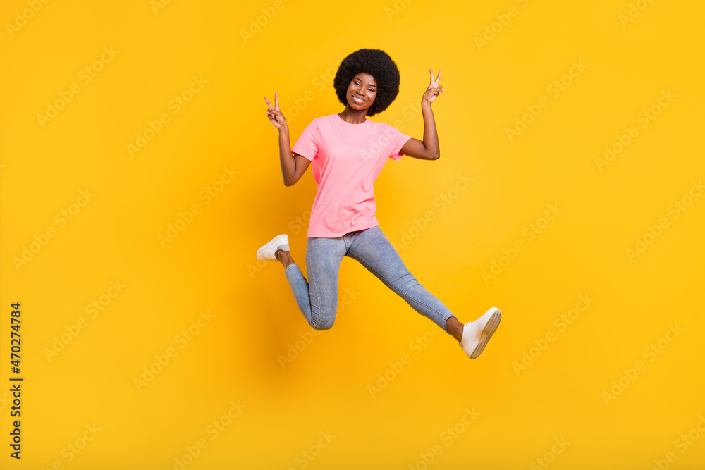 Full body photo of sweet millennial lady jump show v-sign wear pink t-shirt jeans isolated on yellow color background