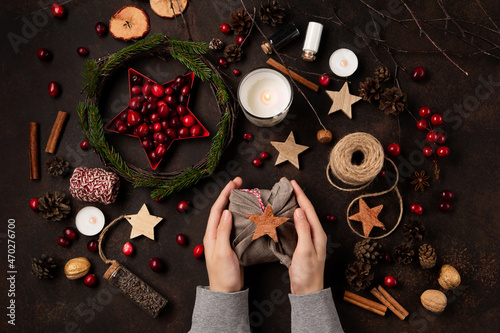 Yule winter solstice concept. Hands holding gift wrapped in linen fabric, tree branches, red berries, candles on wooden background.