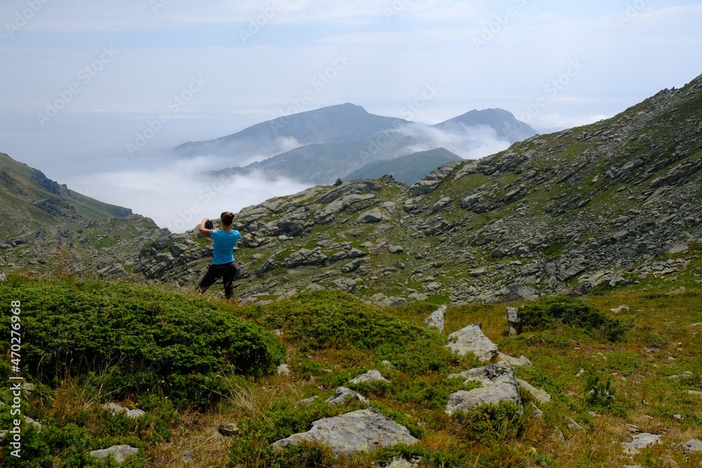 Beautiful mountain view above clouds during hiking on peak Djeravica (Gjerovica) - highest peak of Kosovo. Silhouette of woman taking photo on viewpoint. Albanian Alps, Peaks of Balkans