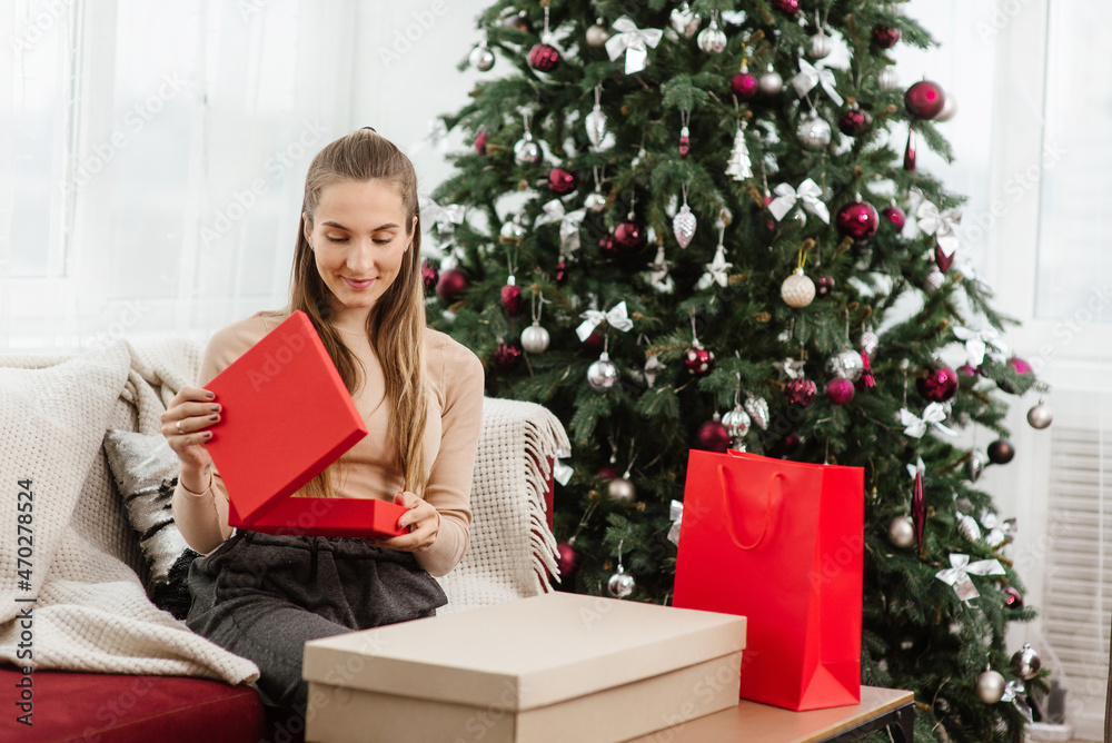 Holidays, celebration and gift project. Smiling woman with red gift box over Christmas tree background Holidays, celebration and gift project. Smiling woman with red gift box over Christmas tree background