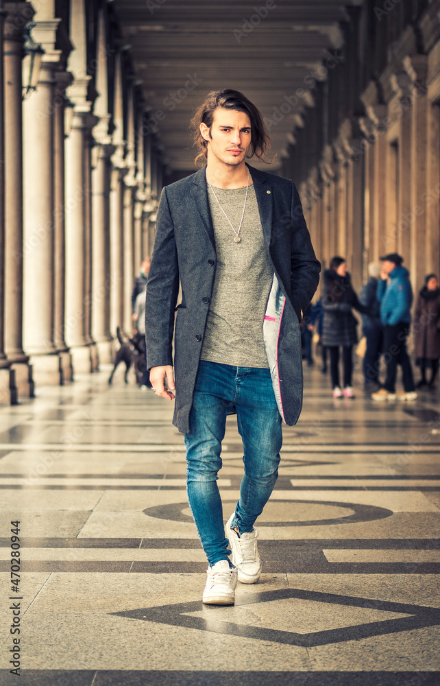 Elegant young man outdoor wearing wool coat and jeans under colonnade