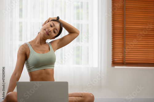 In the fitness studio, an Asian woman is studying online fitness training. Improve your health by extending your neck and meditating.
