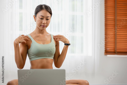 In the fitness studio, an Asian woman is studying online fitness training. Improve your health by extending meditating.