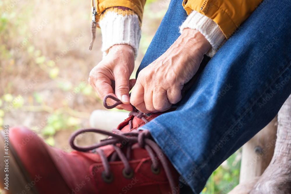 Closeup of woman tying boot shoe laces. Female enjoying hiking getting ready for outdoors excursion. Red boot and yellow jacket