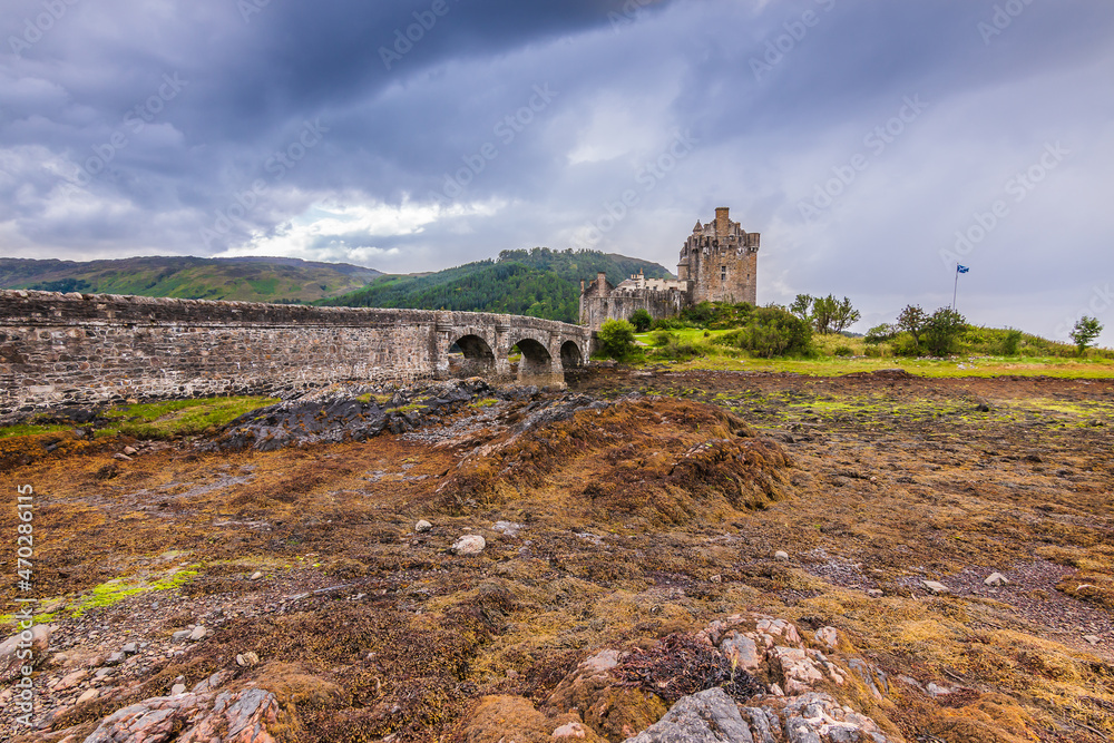 Eilean Donan Castle in Scotland on an island at low water. Historic stone footbridge with stone arches at low tide. Stones with algae and grass in the foreground