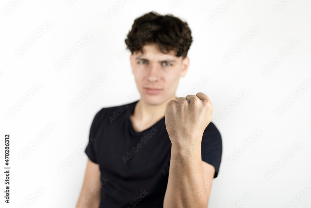 The young man holds a fist in front of him and threatens someone, the focus is on the fist, the face is blurred, the guy believes that force and not dialogue can solve the problem