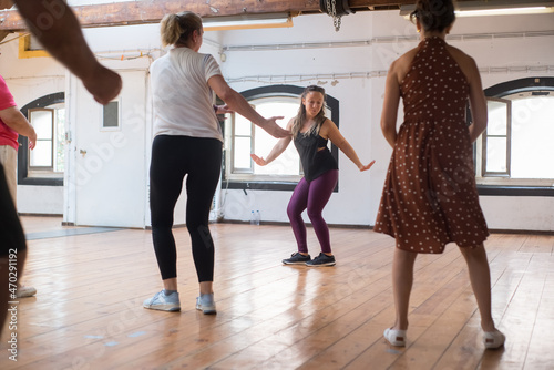 Happy young instructor teaching twist dance steps. Female Caucasian teacher with long fair hair demonstrating twist to her senior group in studio. Dance, hobby, healthy lifestyle concept photo