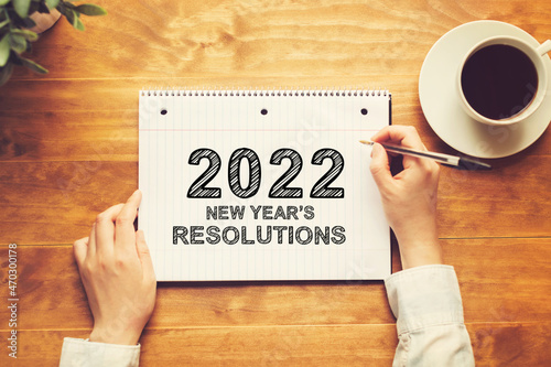 2022 New Years Resolutions with a person holding a pen on a wooden desk