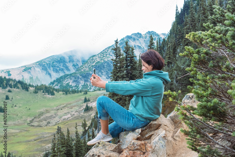 Woman holding mobile phone and taking photos of nature at mountains viewpoint. People taking selfie.