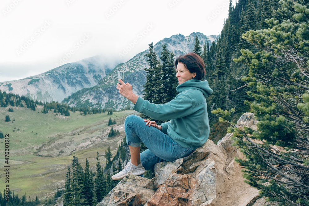 Woman holding mobile phone and taking photos of nature at mountains viewpoint. People taking selfie.