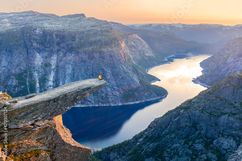 Amazing nature view with Trolltunga and a man sitting on it at sunset under the moon. Location: Scandinavian mountains, Norway, Odda. Artistic image. The world of beauty.  photo