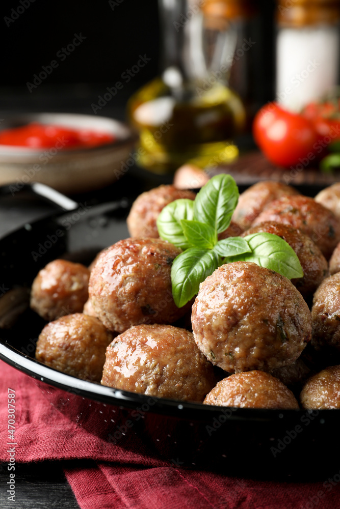 Tasty cooked meatballs with basil on black wooden table, closeup