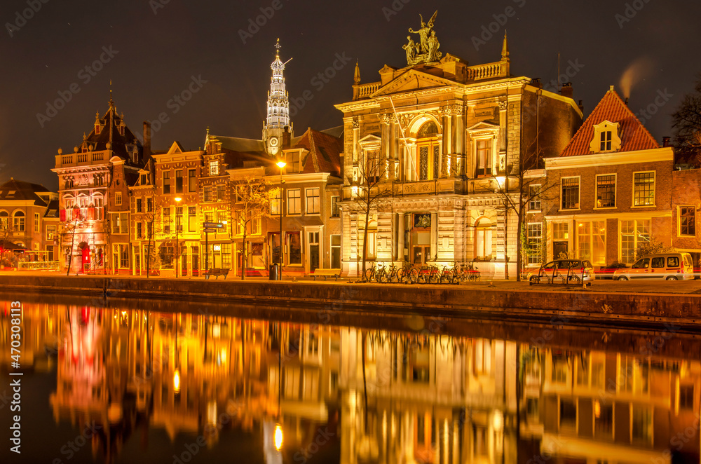 Haarlem, The Netherlands, November 19, 2021: historic facades reflect in the water of Spaarne river at night, with in the background the tower of Saint Bavo's church