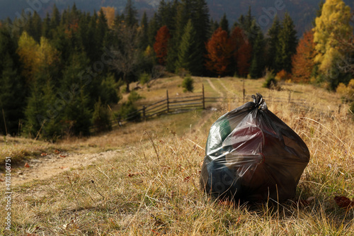 Trash bag full of garbage on ground against beautiful forest. Space for text