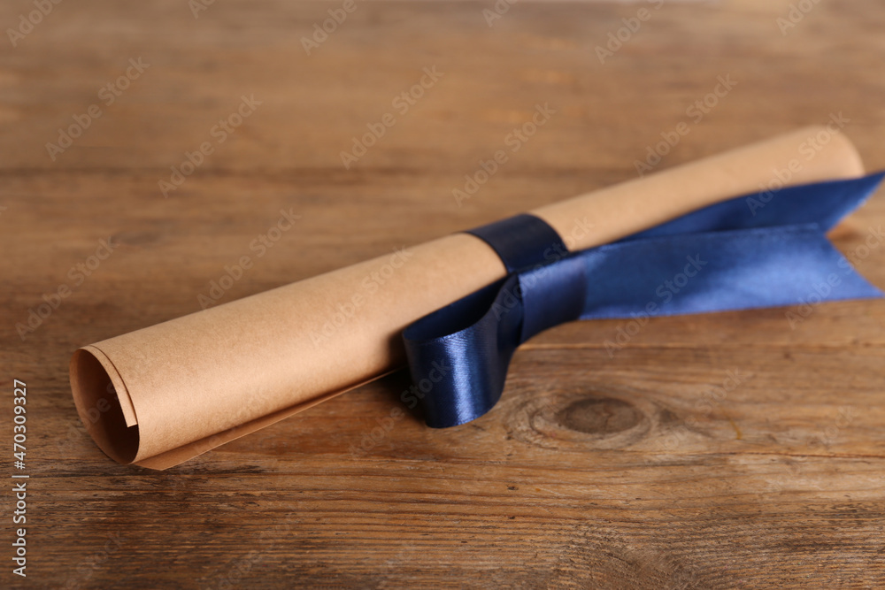 Rolled student's diploma with blue ribbon on wooden table