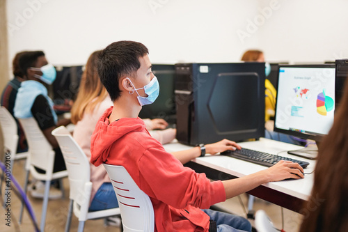 Young people studying inside computer class room - Multiracial students wearing safety face mask for coronavirus outbreak