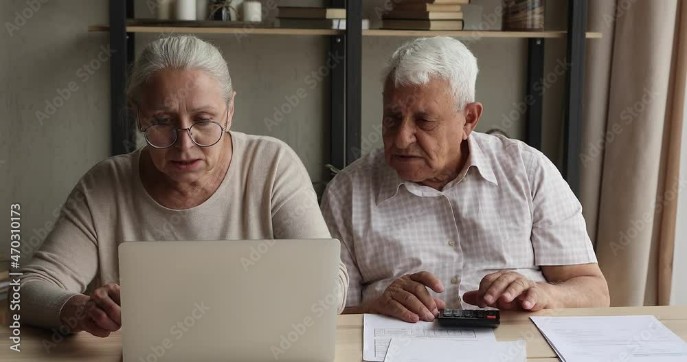 Mature husband wife engaged in paperwork think on monthly budgeting discuss investment pay bills using web banking service on modern laptop pc. Busy aged family couple manage finances at home office Mature husband wife engaged in paperwork think on monthly budgeting discuss investment pay bills using web banking service on modern laptop pc. Busy aged family couple manage finances at home office
