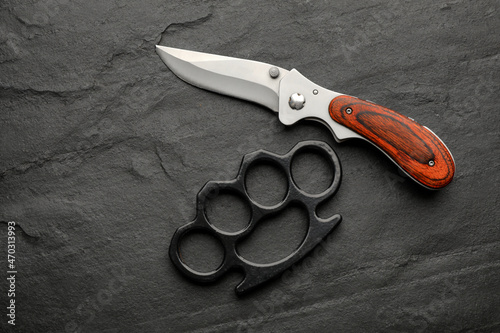 Brass knuckles and knife on black background, flat lay photo