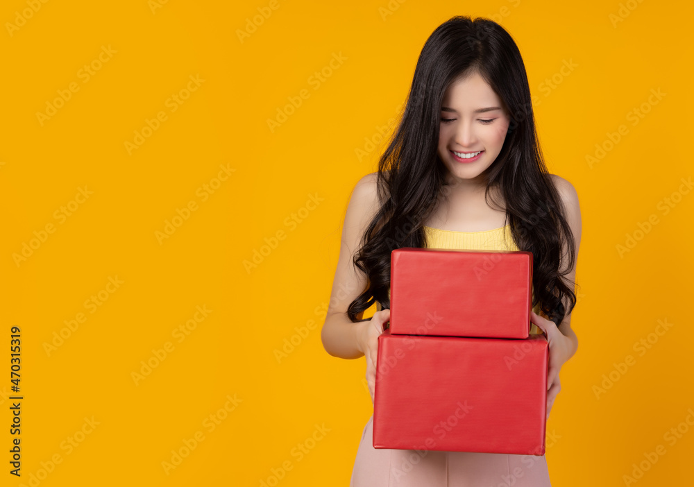 Happy young lady look at red gift box or New year gift box or Christmas present box with smile face and happiness stand over yellow background copy space Christmas day Birthday and New year concept