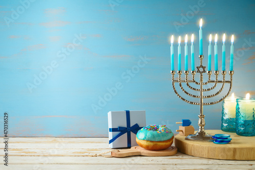 Hanukkah concept with menorah, candles, gift box and traditional donut on wooden table over blue background