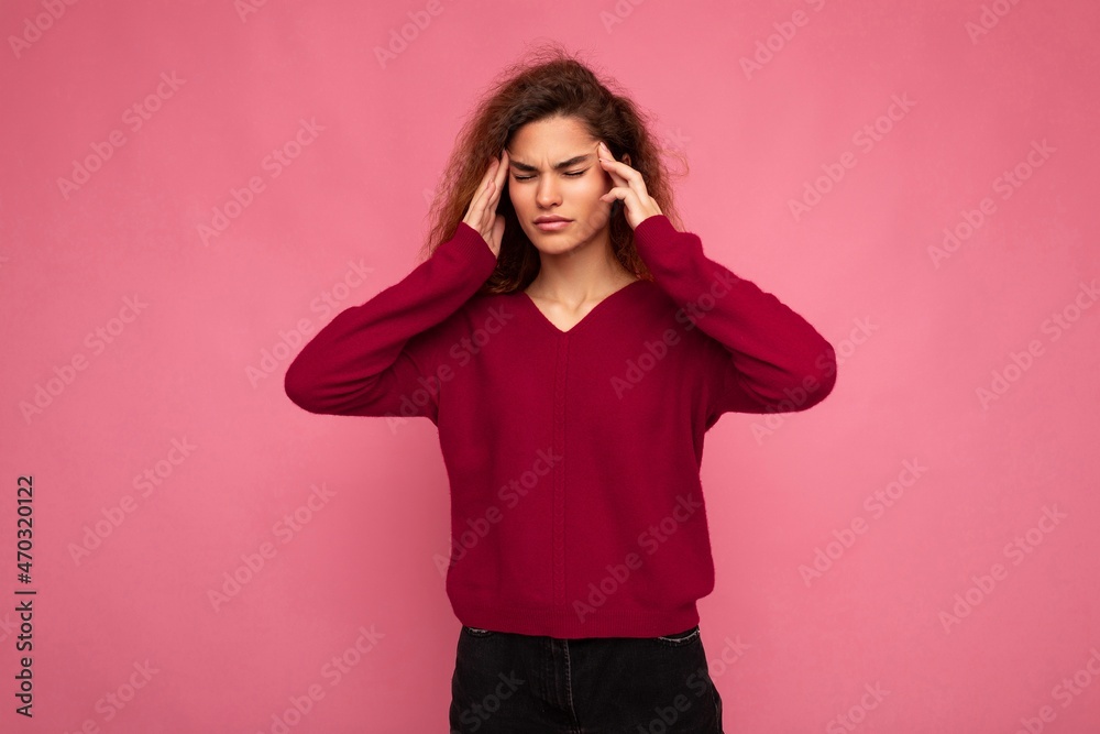 Portrait of young emotional beautiful brunette curly woman with sincere emotions wearing trendy pink pullover isolated on pink background with copy space and having headache Portrait of young emotional beautiful brunette curly woman with sincere emotions wearing trendy pink pullover isolated on pink background with copy space and having headache