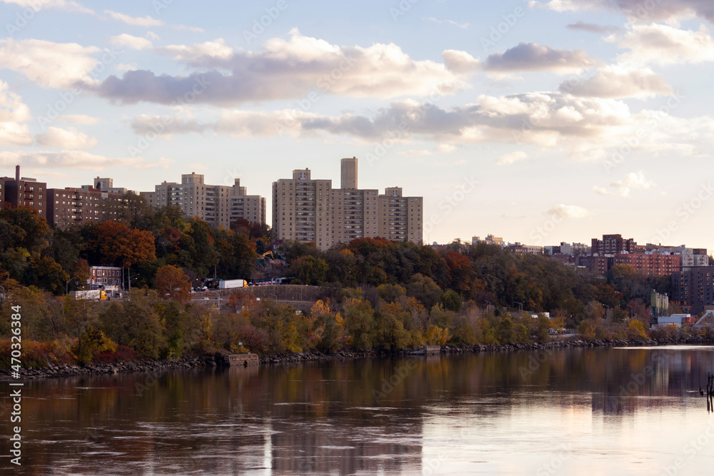 cityscape view of the North Bronx from across the Harlem River at the golden hour, with fall foliage and twilight clouds in the sky